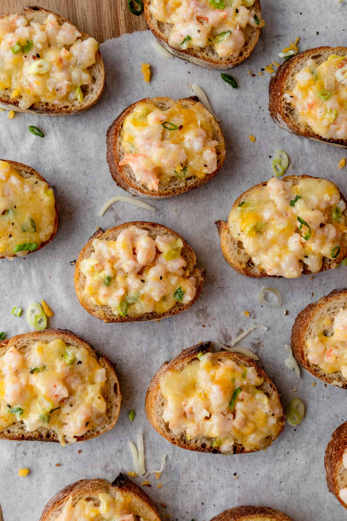 Close up of multiple shrimp toast with green onion and shredded cheese strewn about.