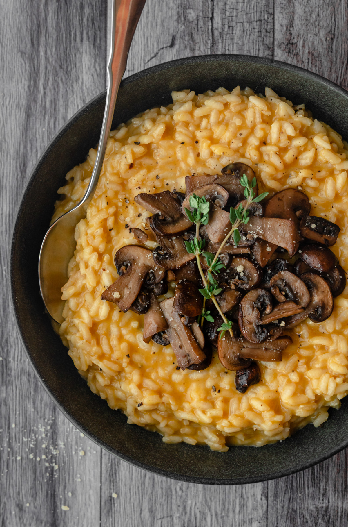 Close up of pumpkin risotto topped with mushroom and thyme sprigs with spoon in it.
