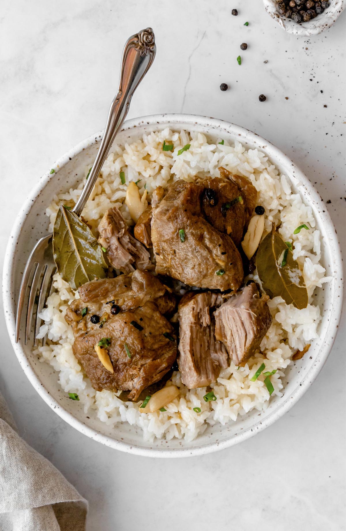Lightly shredded Instant Pot Pork Adobo over a bed of rice in a bowl with a fork.