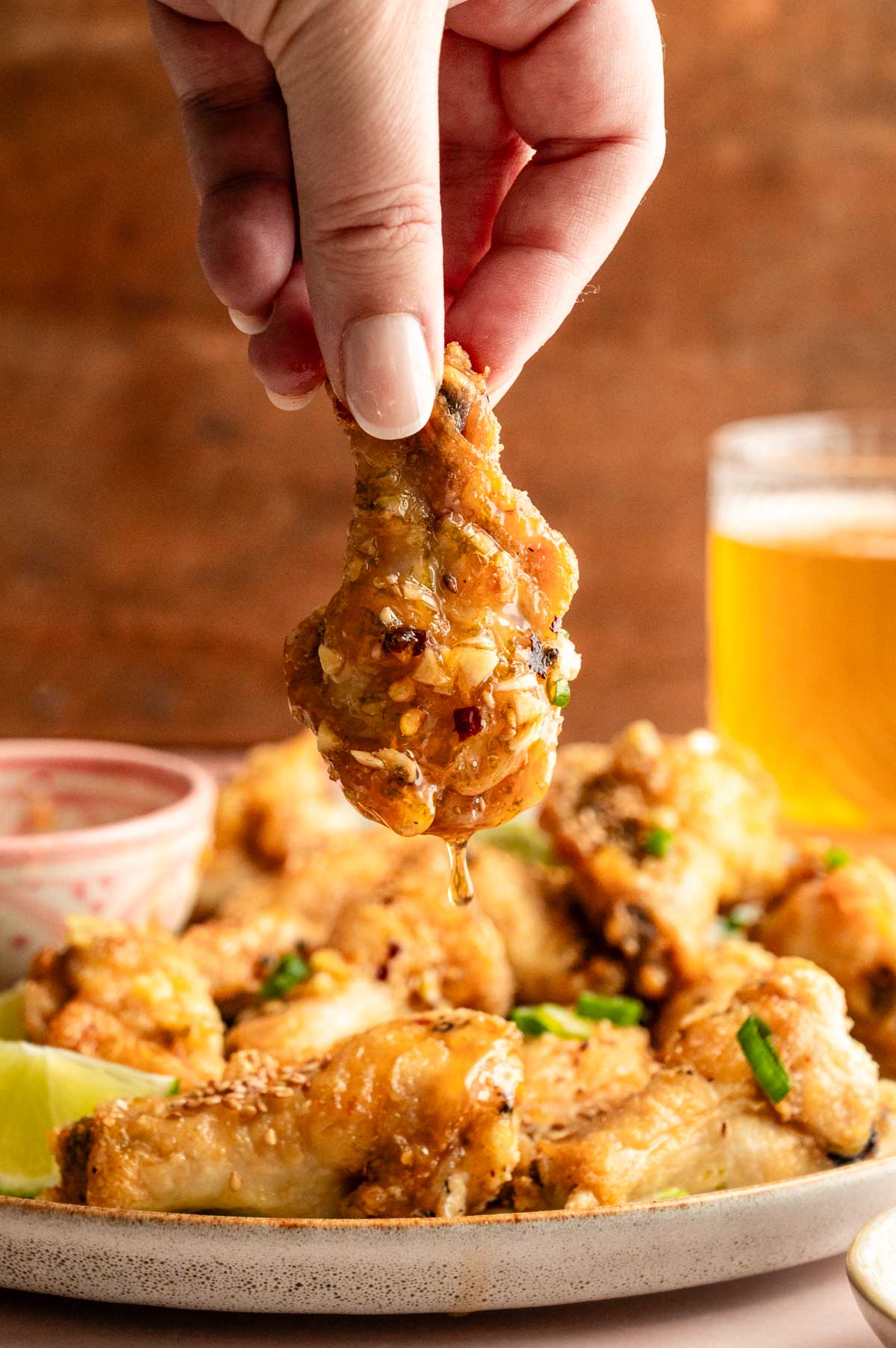 A hand holding up a single chicken drumette with honey dripping off of it.
