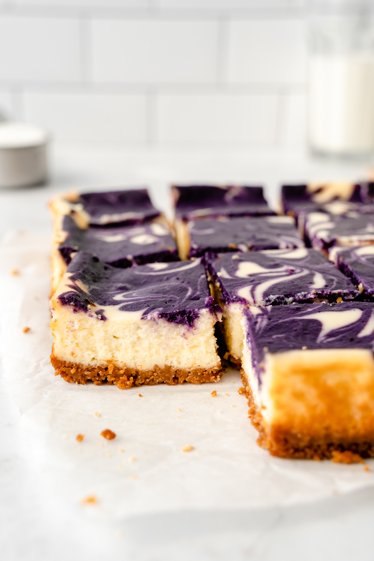 Side view of mini cheesecake squares with glass of milk in the background.