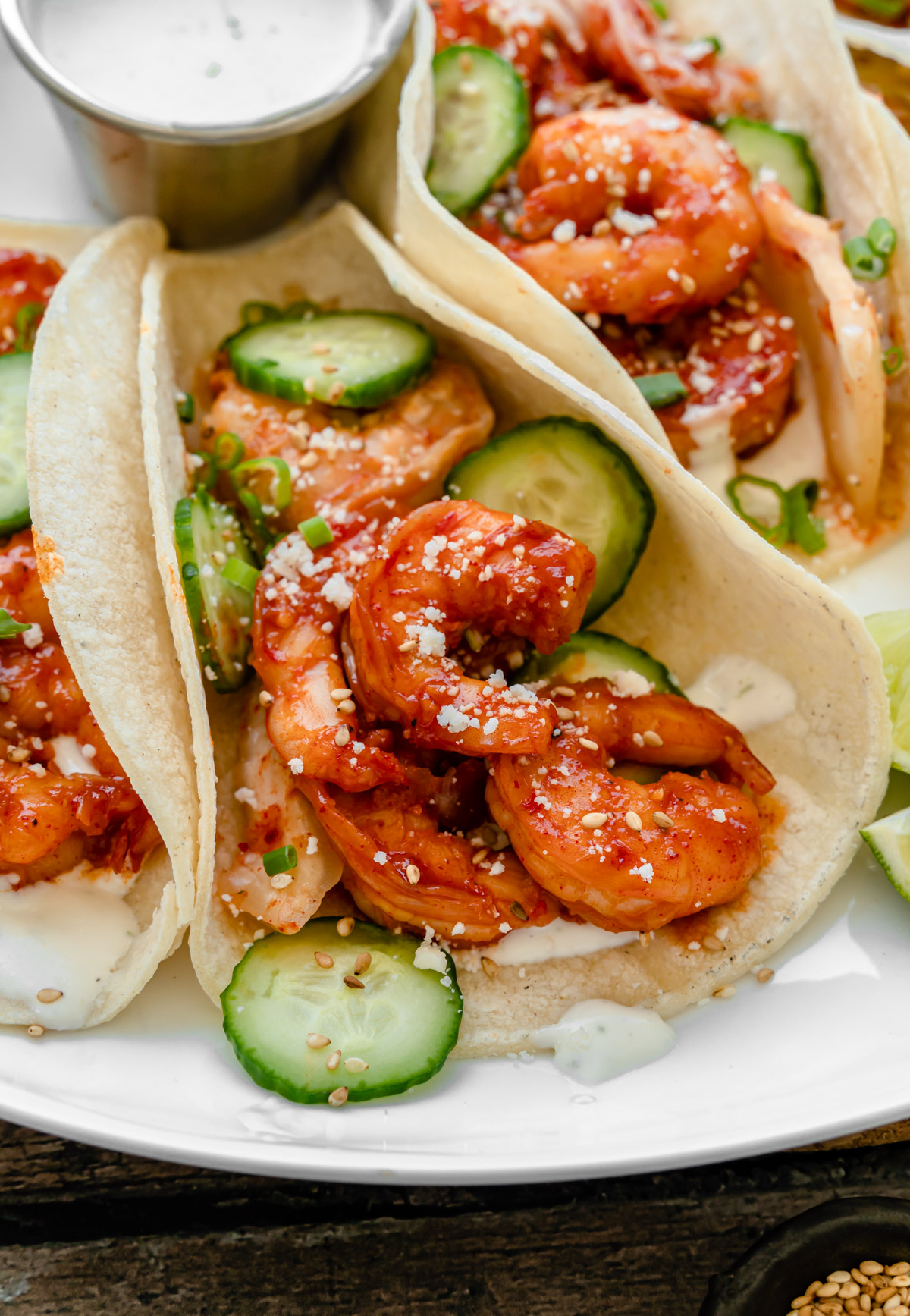 Close up of Korean Shrimp Tacos topped with cucumbers, sesame seeds, cotija cheese, and green onion.