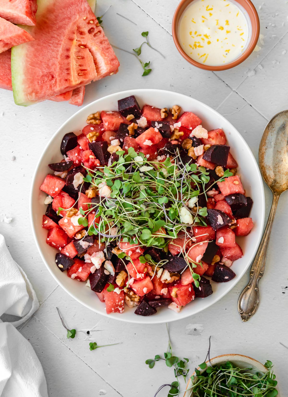 Serving bowl of Watermelon Beet Salad topped with a serving spoon next to it and dressing on the side.