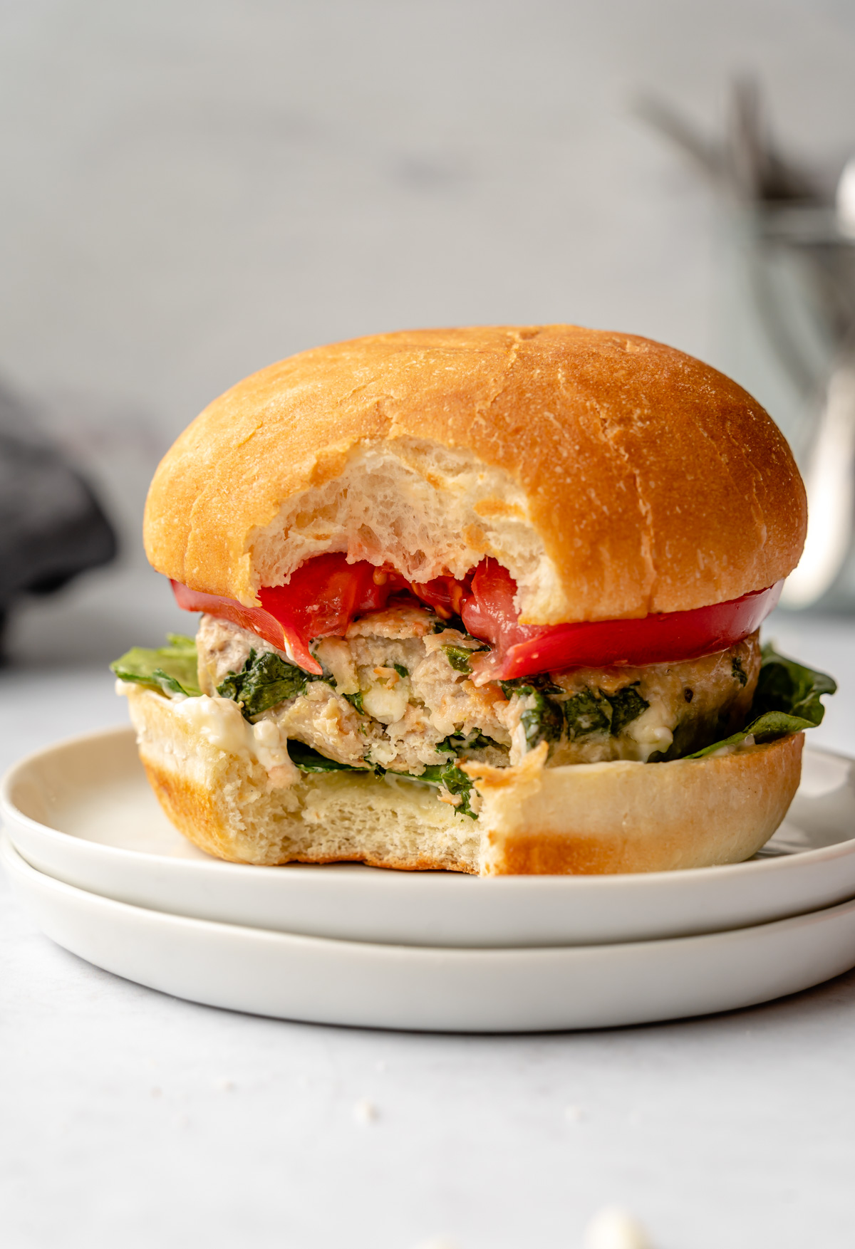 Chicken feta spinach burger on top of plates with a bite in it.