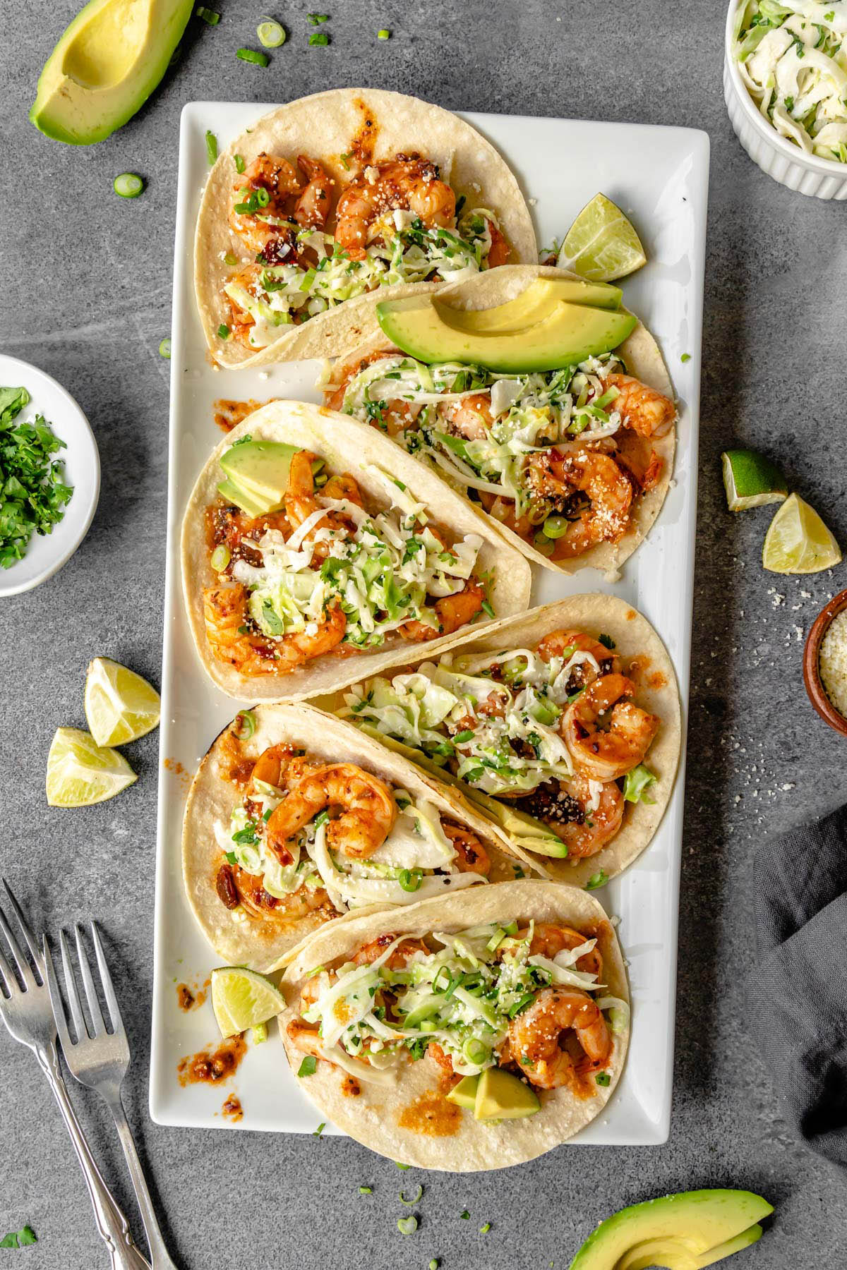 Six honey chipotle shrimp tacos on a platter surrounded by garnishes.
