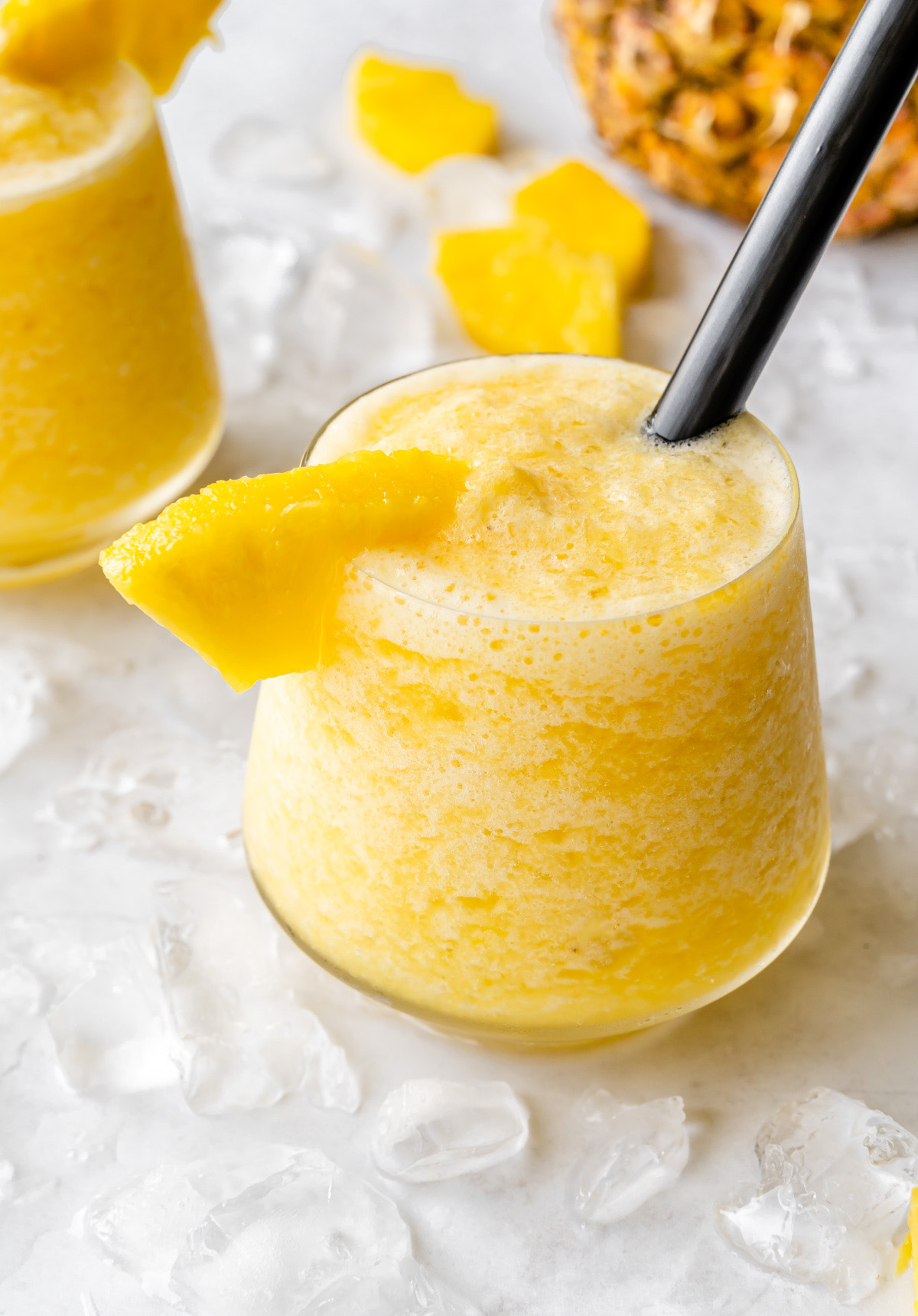 Cup of pineapple slushie with a black straw and pineapple garnish.