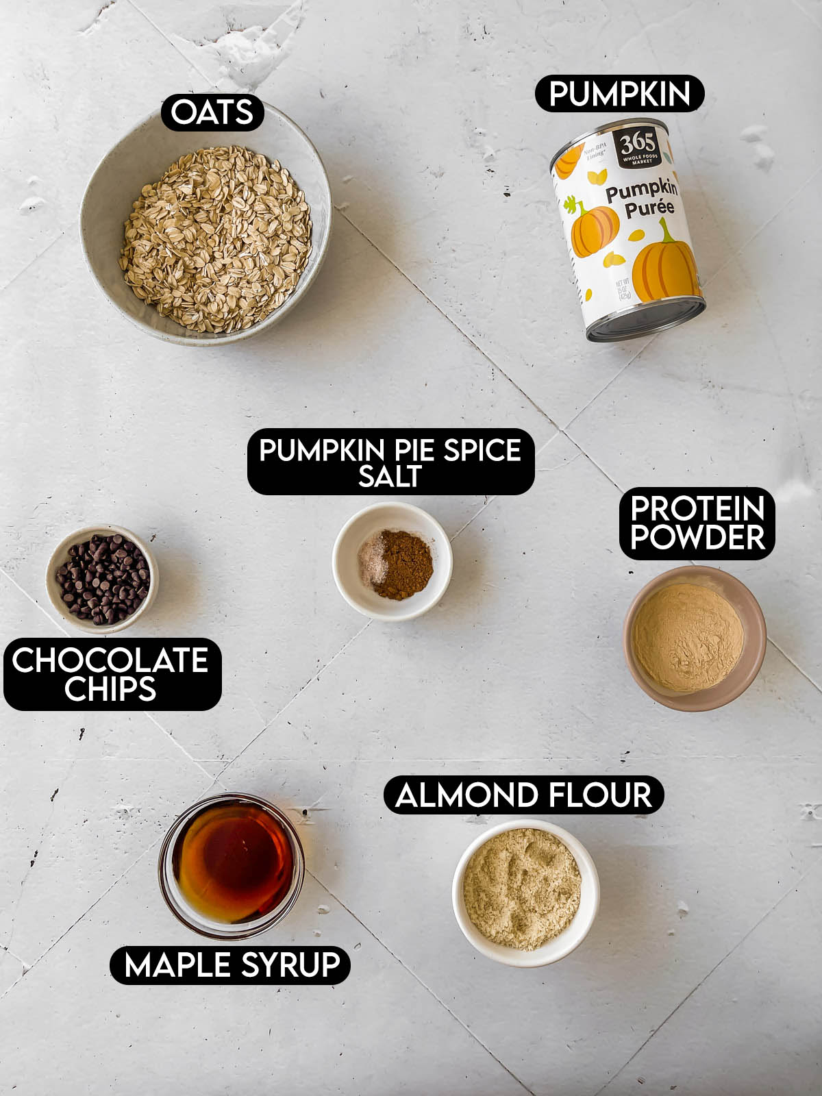 Labeled ingredients needed for Pumpkin Protein Balls: oats, pumpkin, chocolate chips, pumpkin pie spice, salt, protein powder, maple syrup, and almond flour.