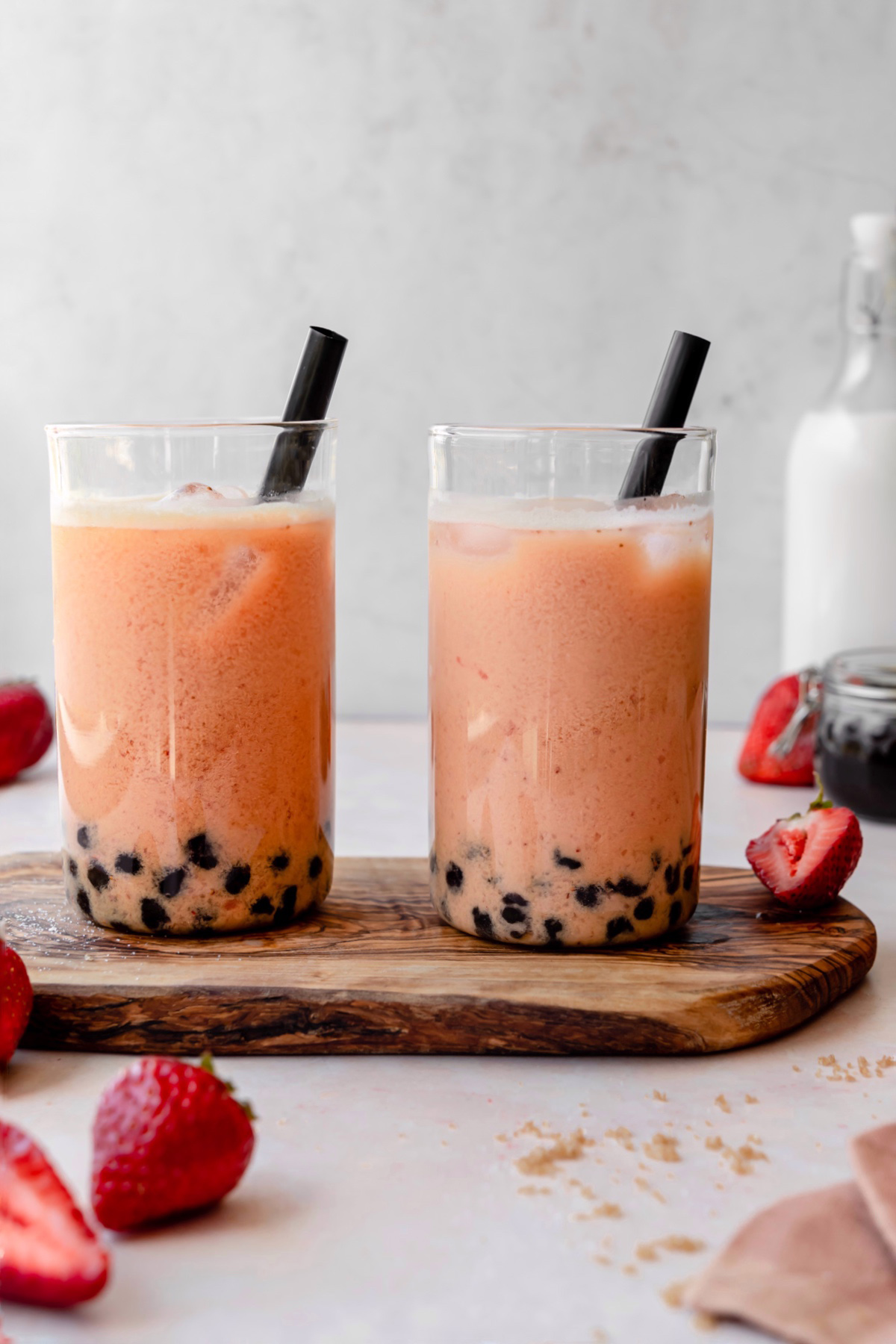 Glasses of strawberry bubble tea with milk and boba in the background.