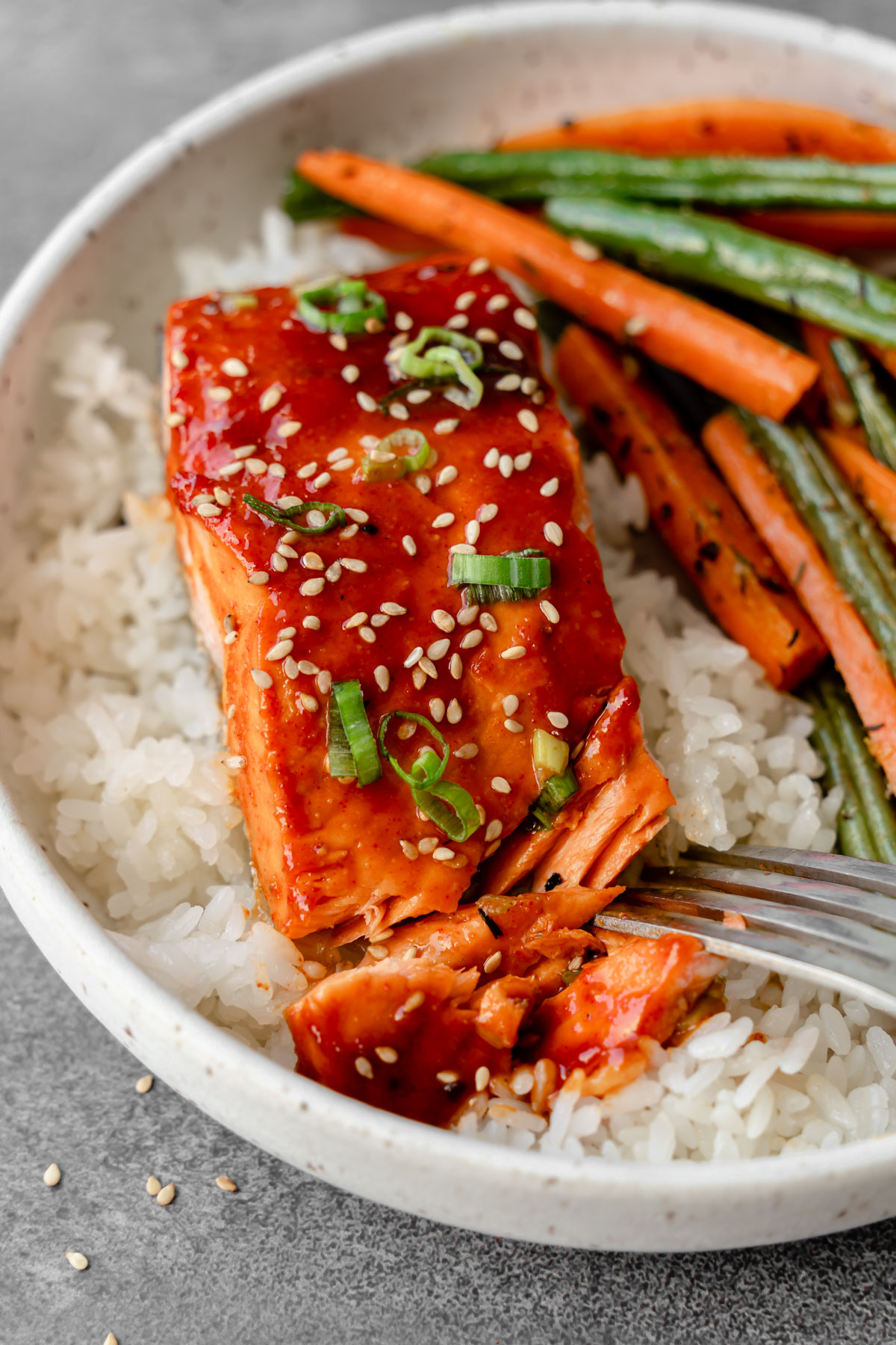 Gochujang glazed salmon in a bowl with rice, roasted vegetables, and a fork.