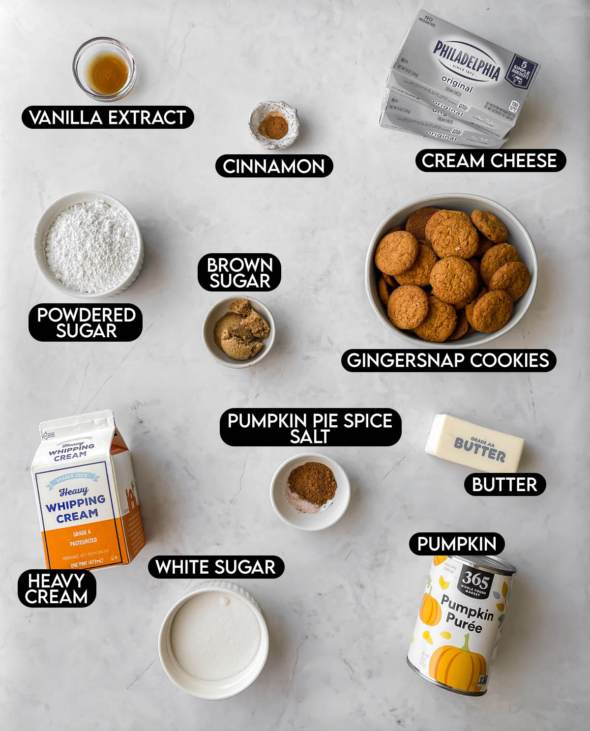 Labeled ingredients for pumpkin cheesecake: vanilla extract, cinnamon, cream cheese, powdered sugar, brown sugar, gingersnap cookies, pumpkin pie spice, salt, butter, heavy cream, white sugar, and pumpkin.
