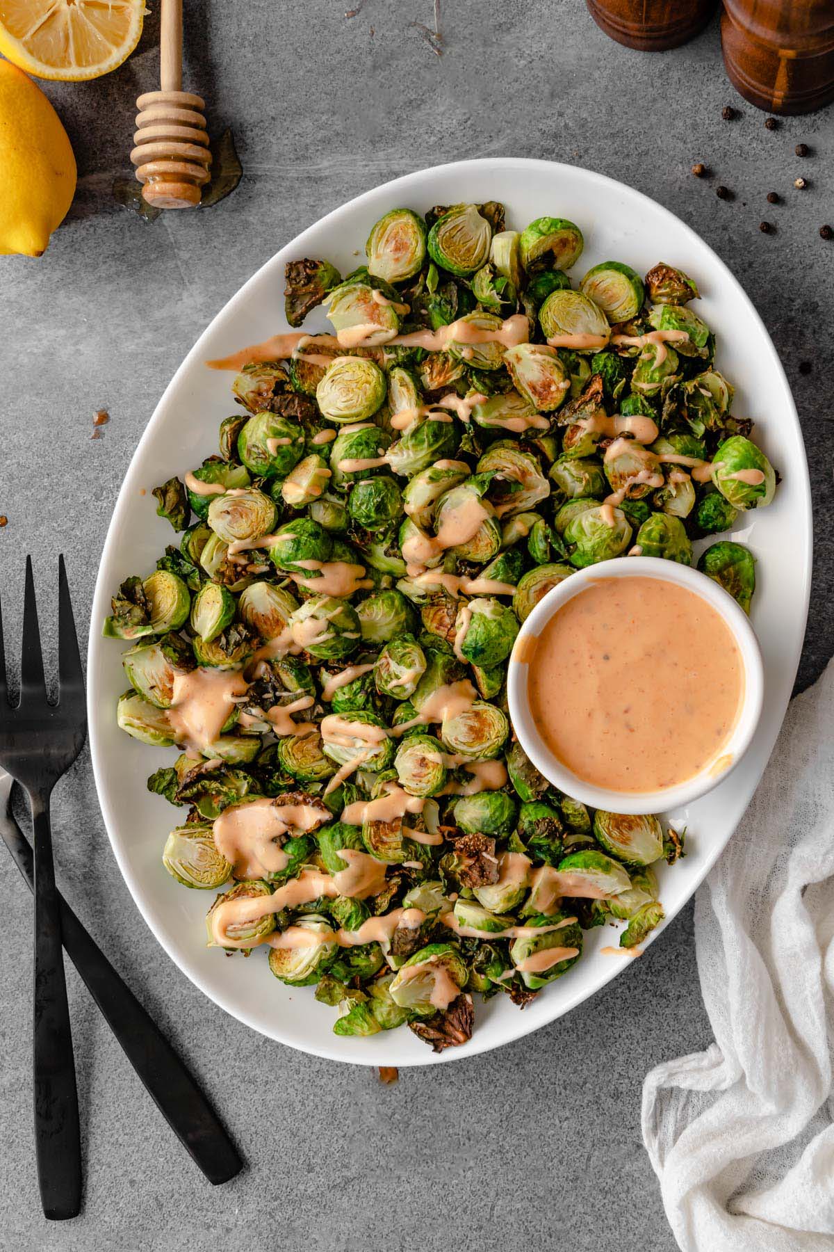 A platter of roasted brussels sprouts with a bowl of bang bang sauce.