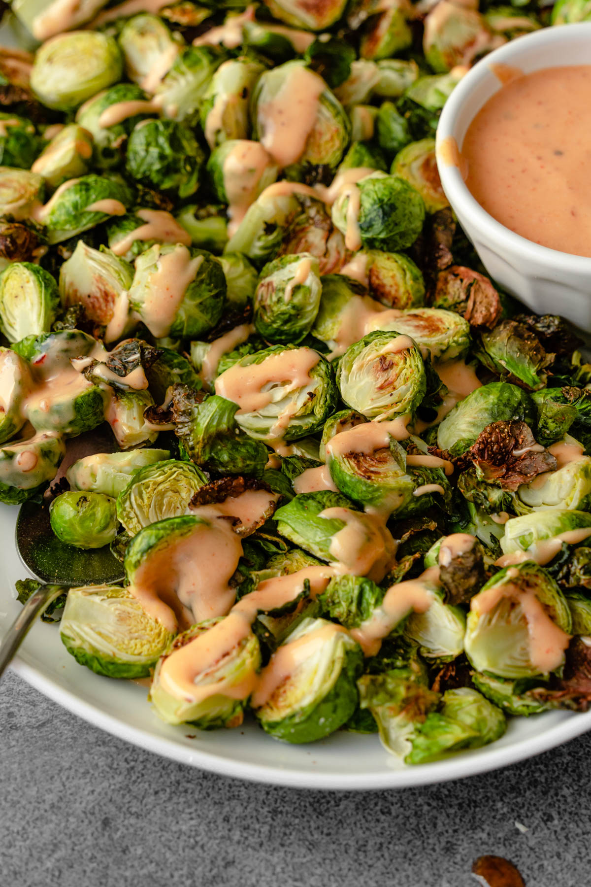 A close up of a spoon going into a platter of brussels sprouts drizzled with bang bang sauce.