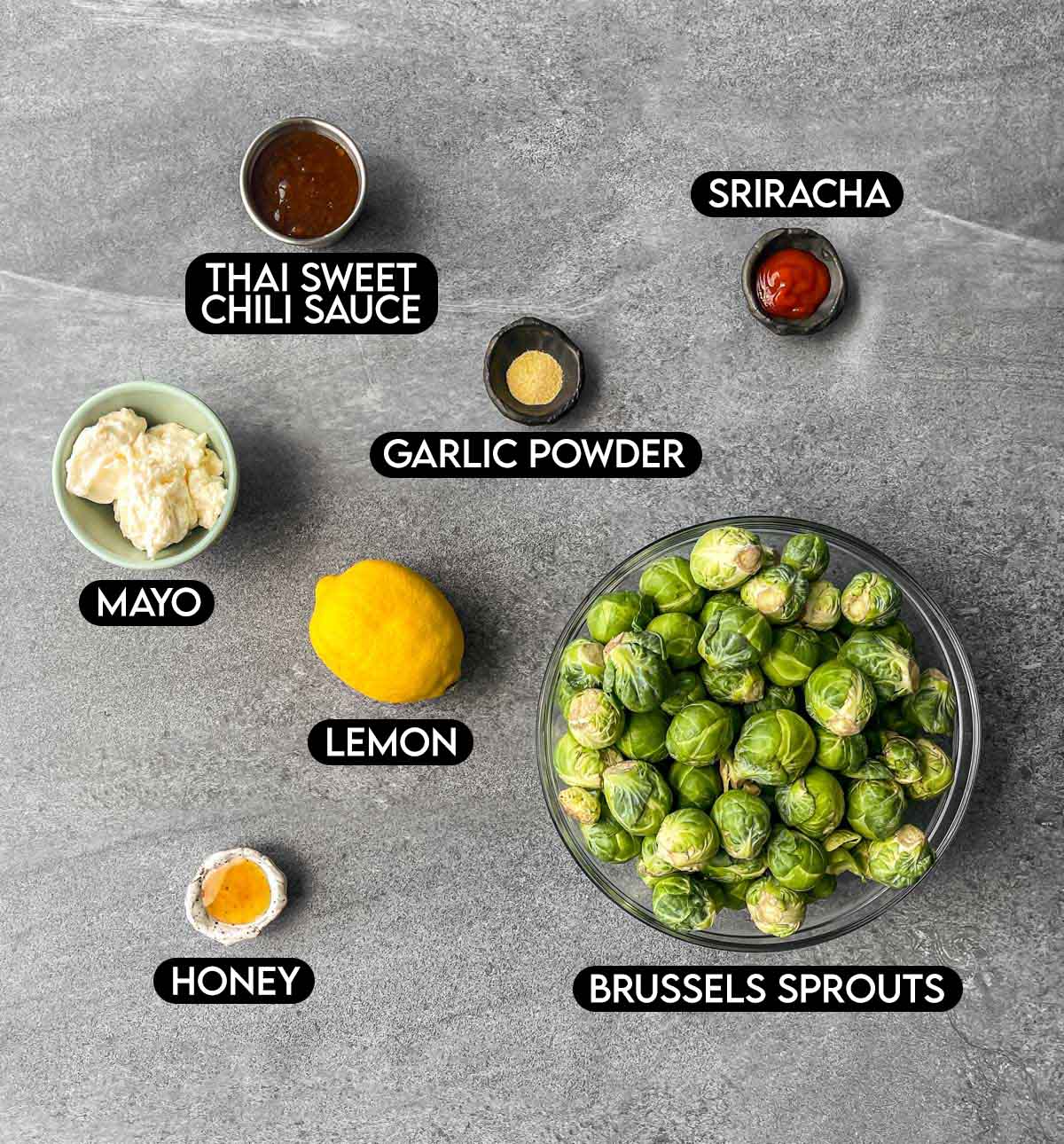 Labeled ingredients for bang bang brussels sprouts: thai sweet chili sauce, sriracha, garlic powder, mayo, lemon, honey, and brussels sprouts.