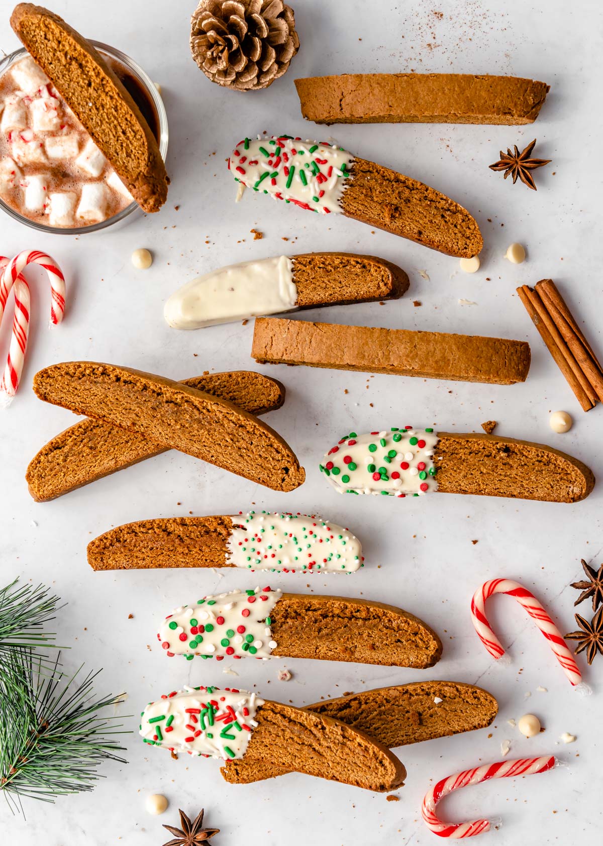 Several gingerbread biscotti, some dipped in white chocolate, and a mug of hot chocolate to the side.