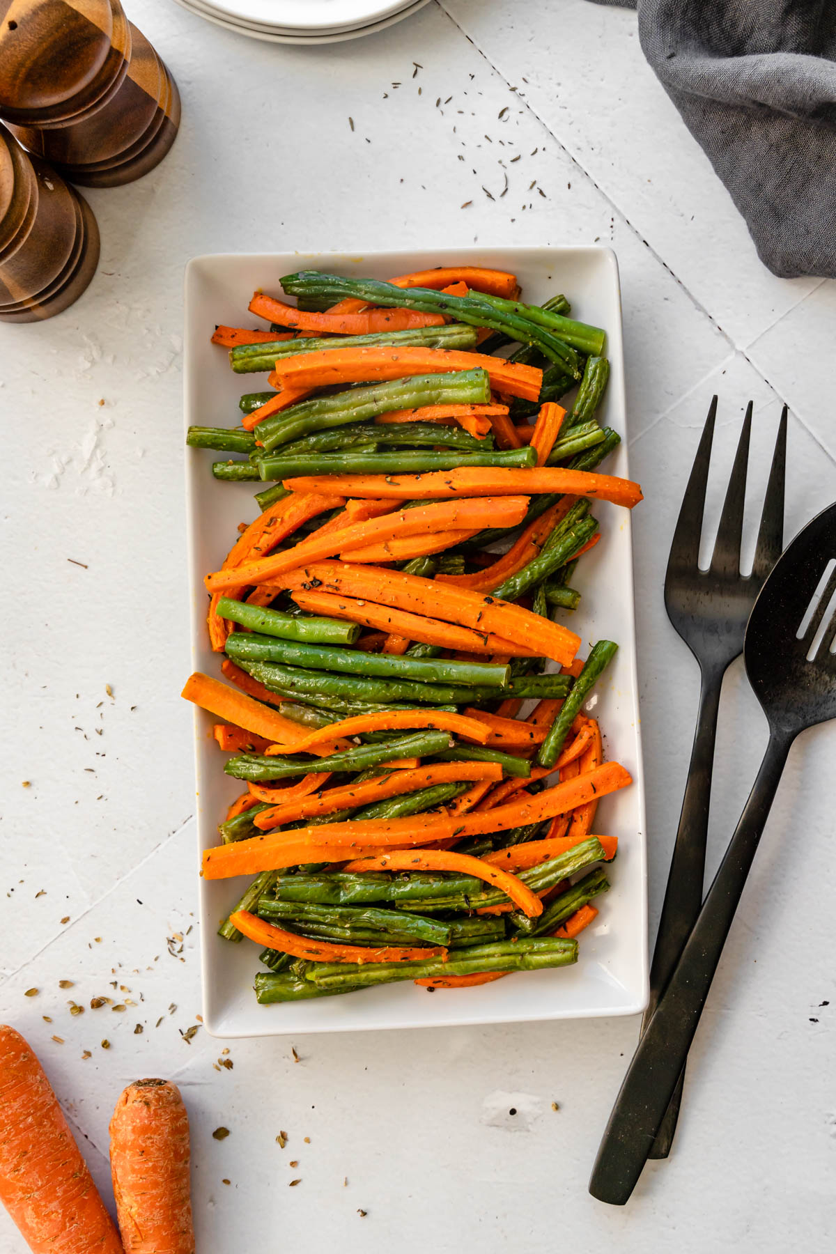 A plate of roasted carrots and green beans with serving utensils on the side.