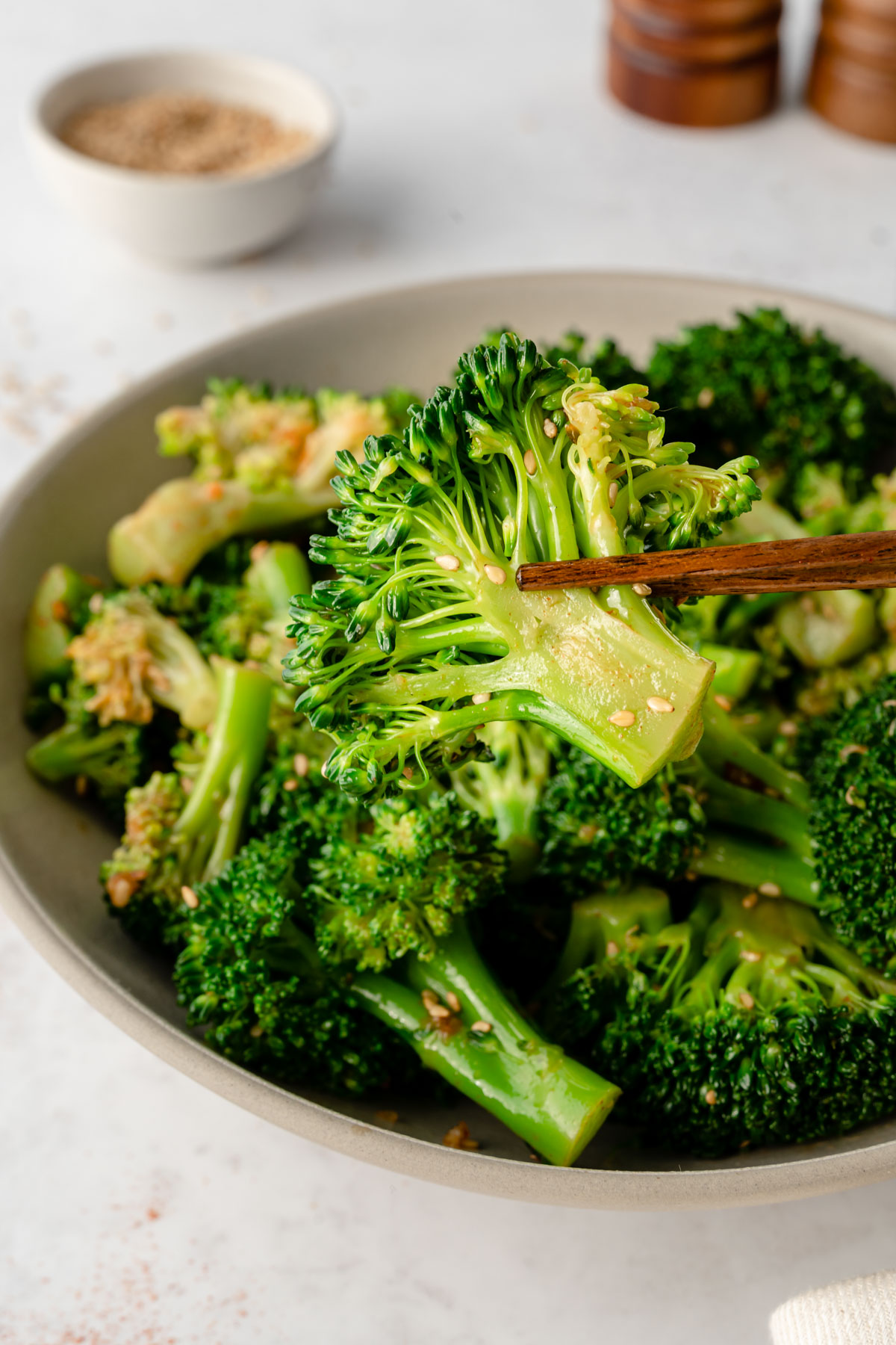 Wooden chopsticks holding a marinaded broccoli over a bowl of Korean Broccoli Salad.