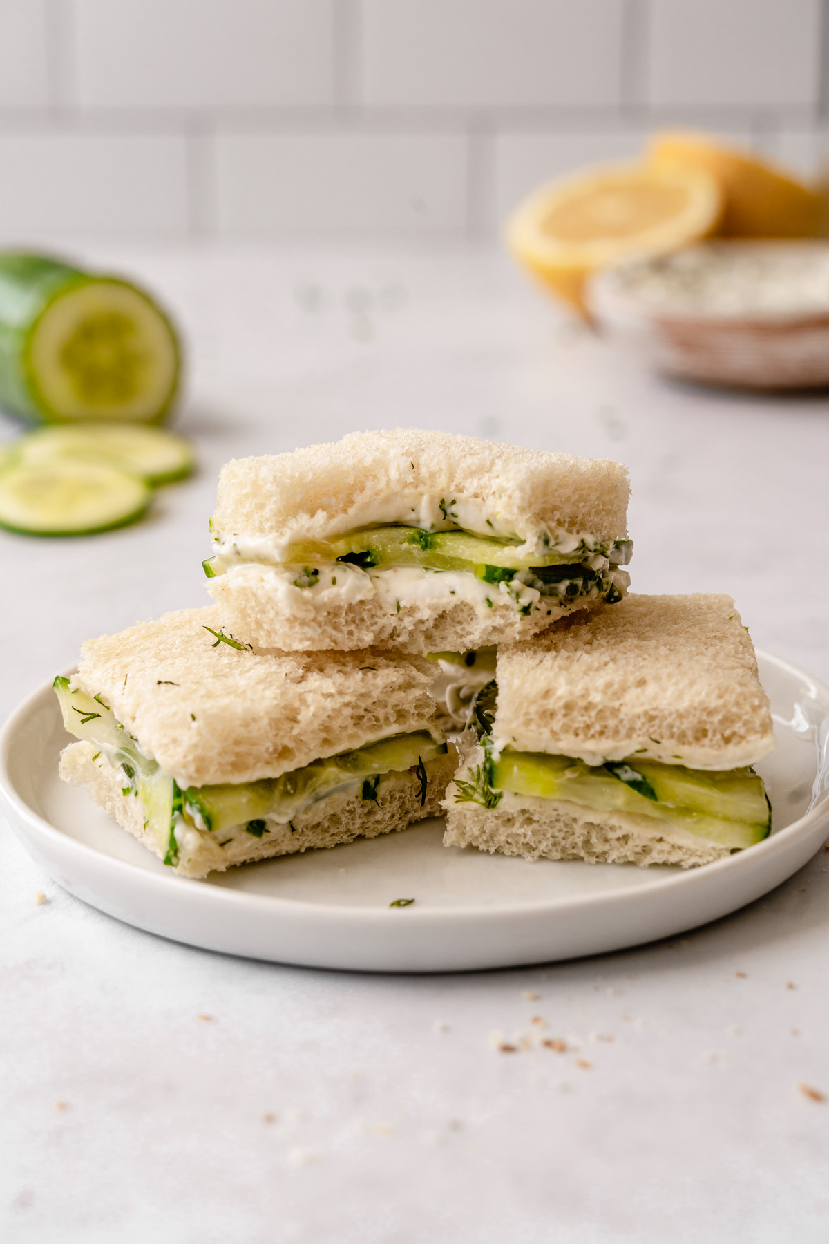 Three cucumber sandwiches stacked on a plate with the top one with a bite.